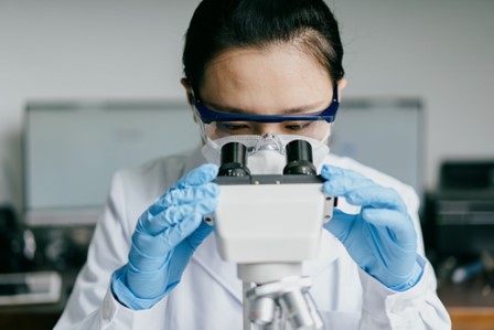 Une femme en blouse blanche portant des gants en latex bleus utilise un microscope.