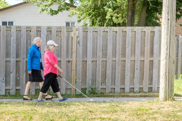 VLRC specialist walks next to woman using a white cane on sidewalk 