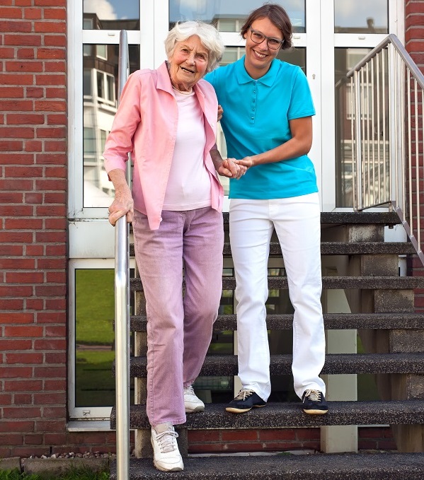 A female health care worker guides an older woman down a set of stairs