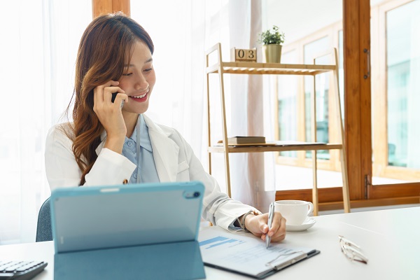 A female medical professional sits at a desk while talking on the phone.