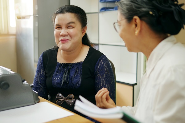 A woman with vision loss sits at a desk with a health care provider