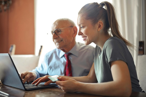 A female health care practitioner sits in front of a laptop with an elderly man next to her