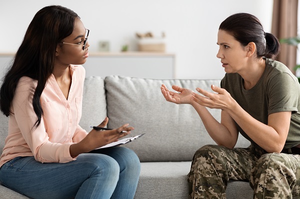 A female mental health counsellor sits on a couch next to a woman wearing military fatigues