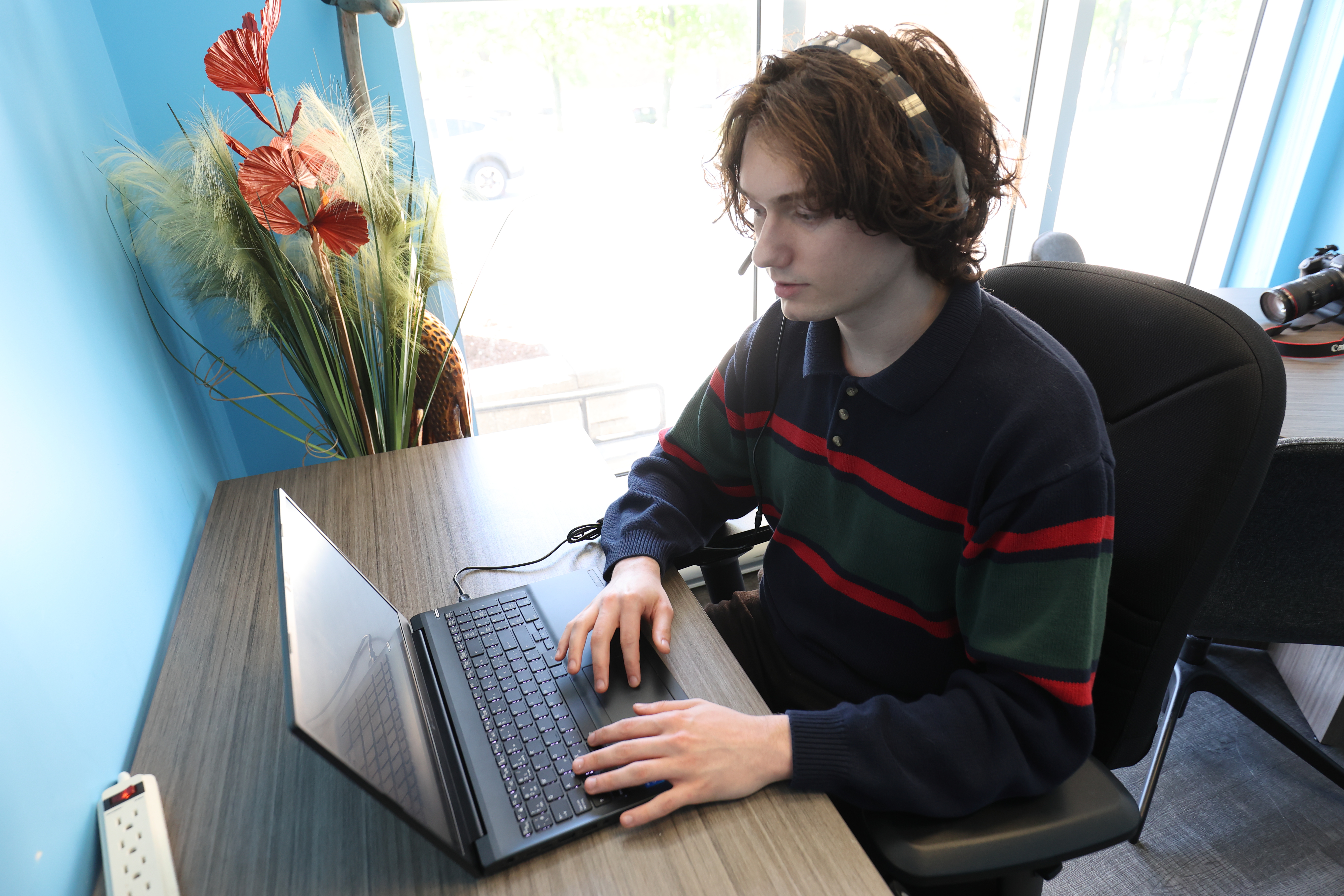 A V.L.R.C. employee is sitting at a desk in the V.L.R.C. office using a computer and headset