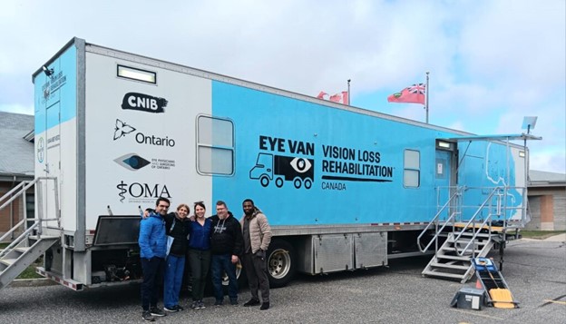 Un groupe de personnes debout à côté d'un semi-remorque bleu et blanc arborant le logo Eye Van.