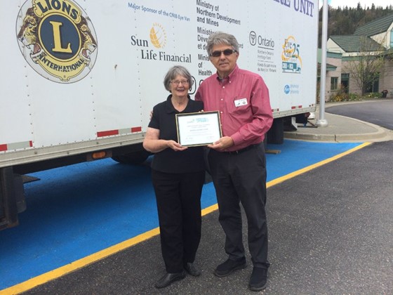 Une femme et un homme tiennent un certificat, debout à côté d'un camion-remorque.