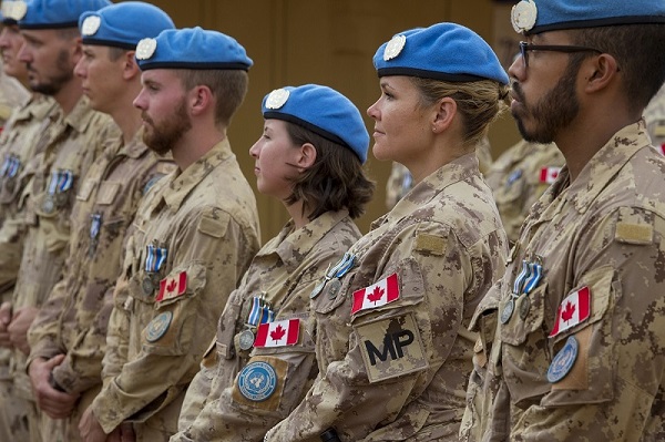 Male and female Canadian peacekeepers wearing beige fatigues and blue berets standing in a line