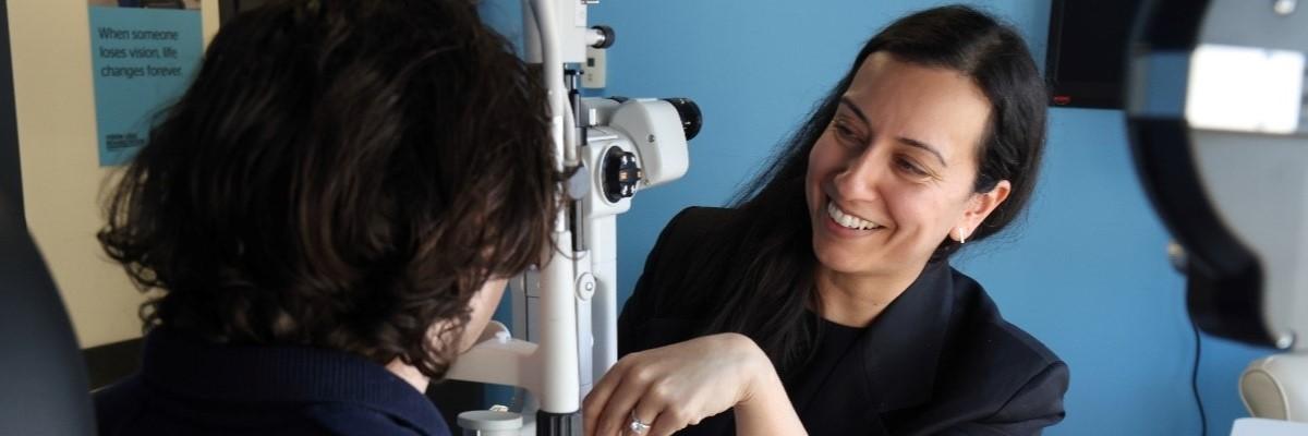 An ophthalmologist conducts an eye examination on a young man in a clinical setting with blue walls and medical equipment.