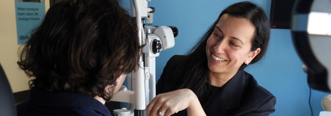 Une ophtalmologiste examine les yeux d'un jeune homme dans un cabinet médical aux murs bleus et équipé de matériel médical.