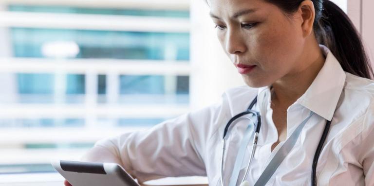 Health care professional looks at tablet, standing by window