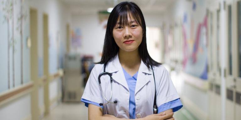 Une professionnelle de la santé se tient debout les bras croisés dans un couloir d’hôpital