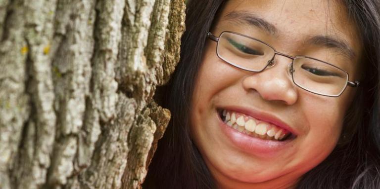 A close-up of a girl climbing up a tree, smiling at the camera