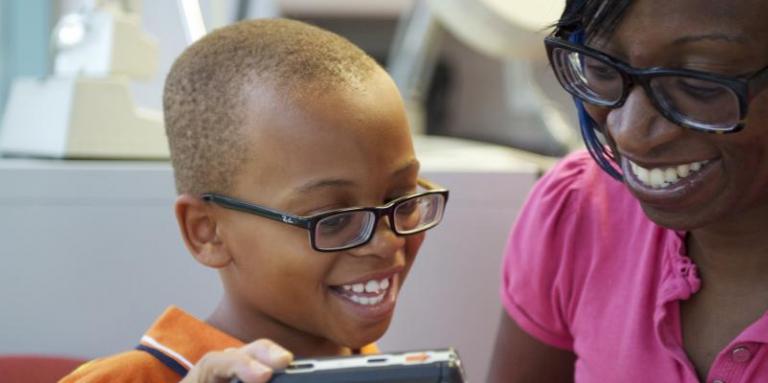 A young boy and his mother, both wearing glasses, interact as the little boy plays with a magnifier. 