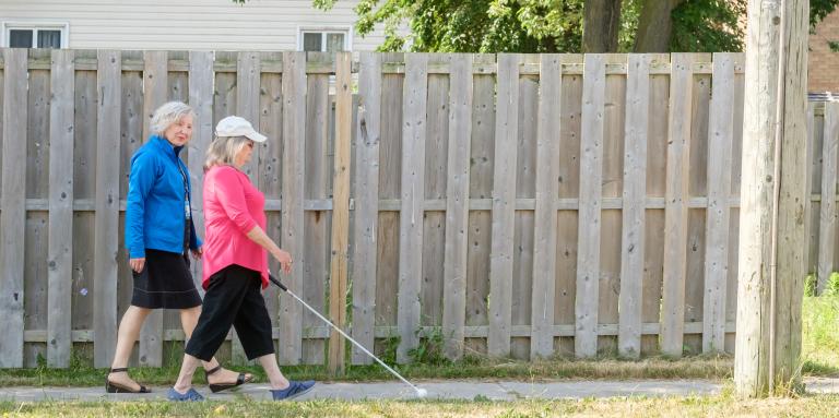 Une spécialiste de RDVC marche à côté d’une femme utilisant une canne blanche sur le trottoir 