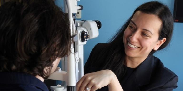 An ophthalmologist conducts an eye examination on a young man in a clinical setting with blue walls and medical equipment.